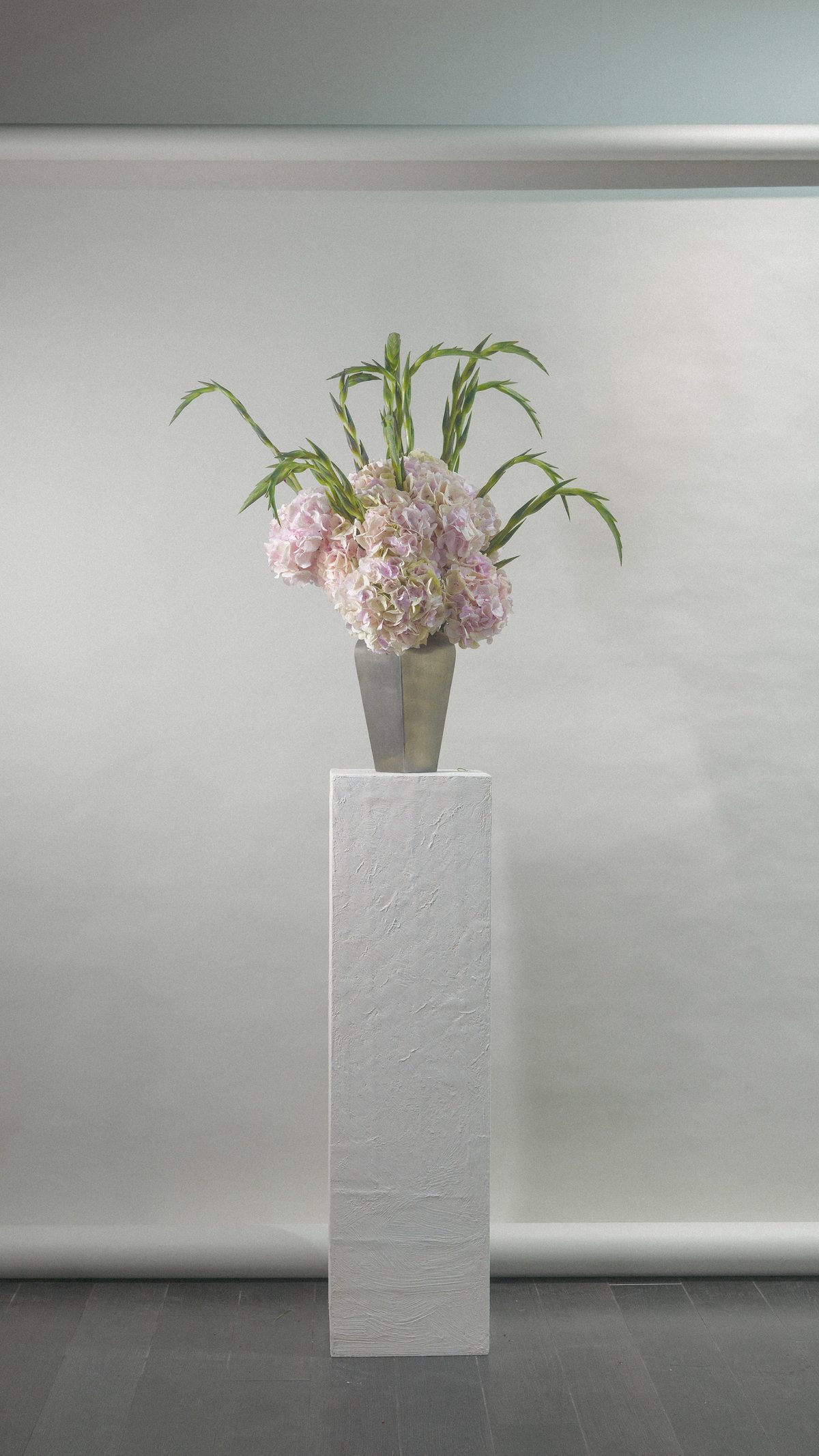Composition FLWR boutique - hortensias roses et glaïeuls dans vase argent sur socle