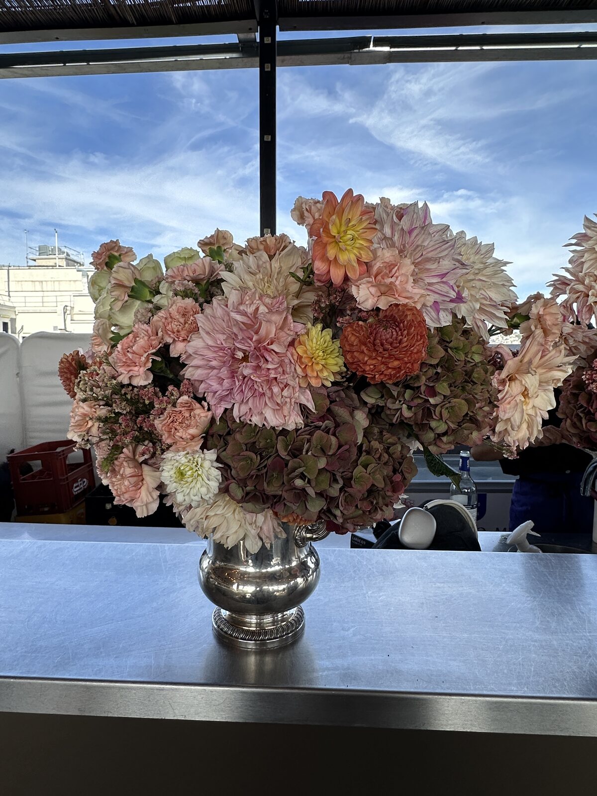 Scénographie florale FLWR Pro pour événement en rooftop, composition de dahlias dans une urne argentée